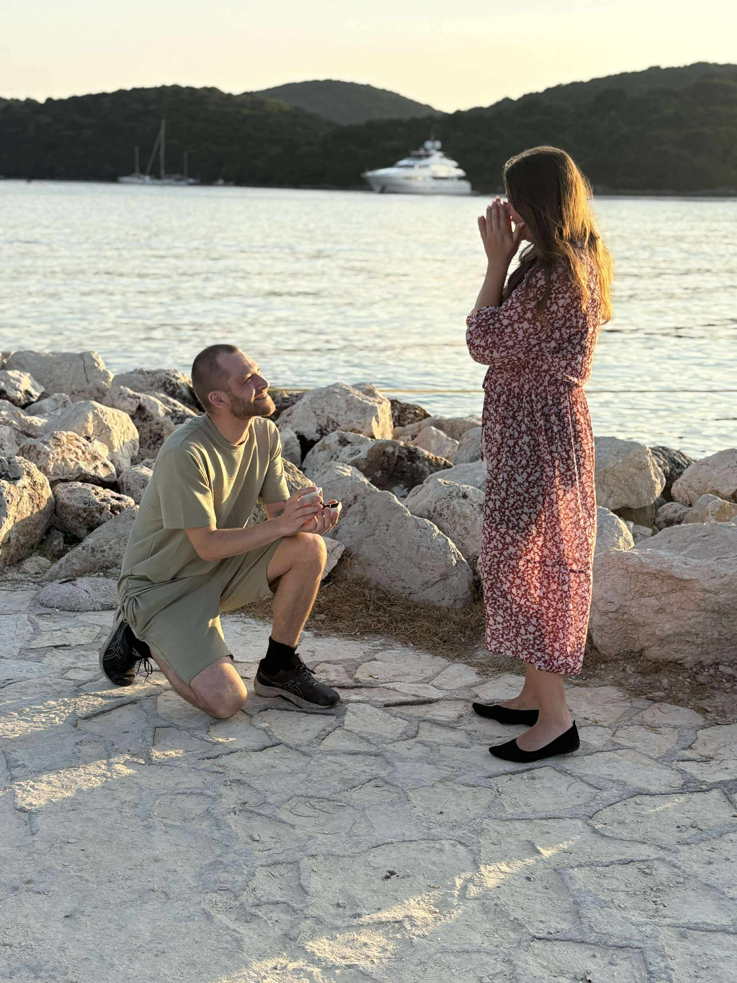 Jocke på knä framför Emelie på klipporna vid vattnet